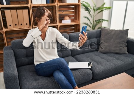 Brunette woman doing online session at consultation office smiling happy doing ok sign with hand on eye looking through fingers 