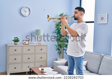 Young arab man musician playing trumpet standing at home Royalty-Free Stock Photo #2238283703