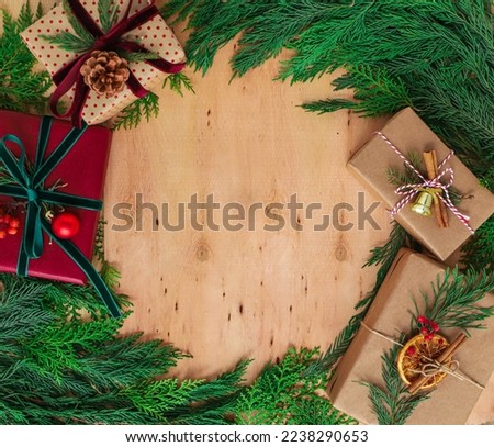 Pine tree branches and Christmas gift boxes rounded on wooden background.