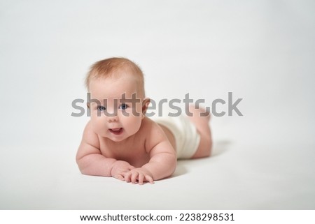 an infant lying on its stomach looking intently into the camera with its mouth open against a white background