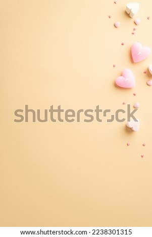 St Valentine's Day concept. Top view vertical photo of heart shaped candles marshmallow and sprinkles on isolated light beige background with copyspace
