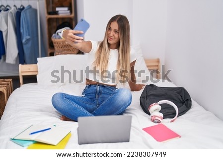 Young beautiful hispanic woman student make selfie by smartphone sitting on bed at bedroom