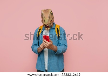 Man with backpack and lizard mask on pink background, he is using the smart phone.