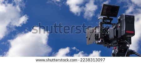 Professional digital film camera on wide blue sky background, movie production or television broadcasting banner with copy space