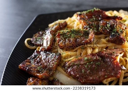 A closeup view of a plate of BBQ short ribs with garlic noodles.