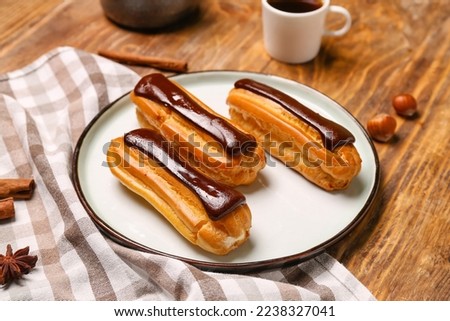Plate with tasty chocolate eclairs on wooden table Royalty-Free Stock Photo #2238327041
