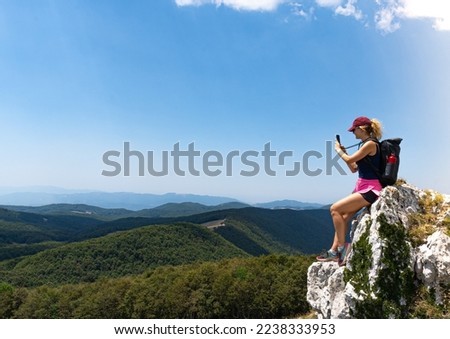 Young woman sitting high in the mountains taking a picture of the view in the background, mountain view