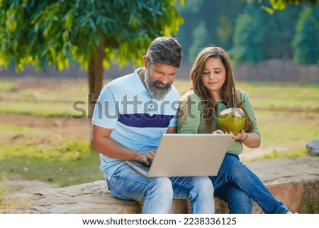 Indian man and woman watching some detail in laptop at park.