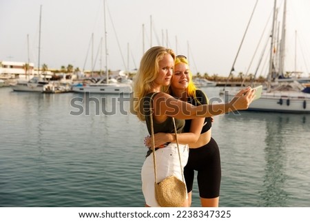 Mother and daughter take selfies against the background of the sea and yachts
