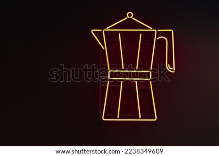 Yellow neon signage in the form of a Moka coffee maker against a black wall