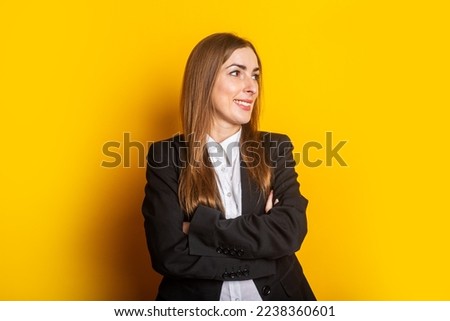 smiling young business woman in a black jacket looks to the side on a yellow background.