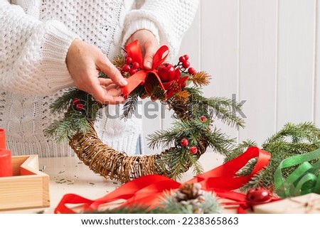 A woman makes and decorates Christmas wreath of spruce branches with red berries colorful ribbons