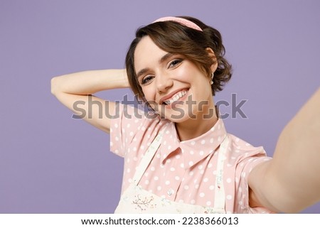 Close up smiling fun happy young housewife housekeeper chef cook baker woman in pink apron doing selfie shot on mobile phone isolated on pastel violet background studio portrait. Cooking food concept.