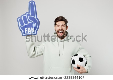 Young excited fun man fan wears mint hoody foam 1 fan glove finger up cheer up support football sport team hold in hand soccer ball watch tv live stream isolated on plain solid white background studio Royalty-Free Stock Photo #2238366109