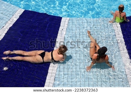 Two young women wearing black bikini and kid girl tanning in transparent water of swimming pool, top view. Hot weather, vacation on sunny resort