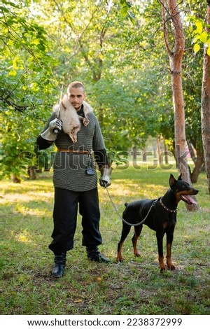A young man in chain mail with a sword in the woods with a dog. A warrior in armor stands with a Doberman on a chain. fantasy image