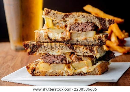 Patty melt sandwich. Ground beef patty with melted cheese and topped with caramelized onions on two slices of griddled rye bread. Classic American meat and cheese Sandwich served with crispy fries. Royalty-Free Stock Photo #2238386685