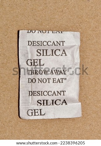 Single Silica gel packet isolated in a cardboard box, flat lay. Porous desiccant substance used in packing material to absorb humidity moisture. Royalty-Free Stock Photo #2238396205