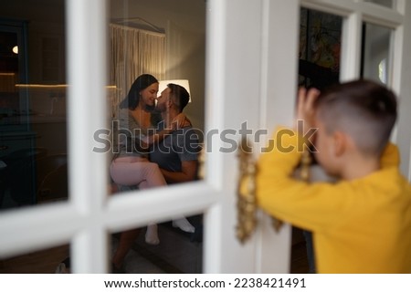Curious child spying on kissing parents looking through window