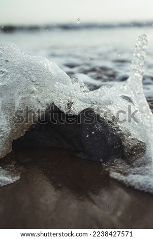 Wave crashing against a small rock on a beach on a grey cloudy day on the Isle of Wight in England. 