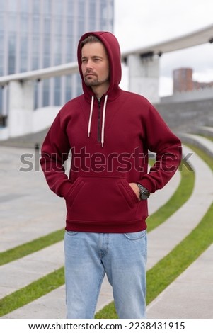 City portrait of handsome hipster guy with beard wearing red blank hoodie or sweatshirt with space for your logo or design. Mockup for print