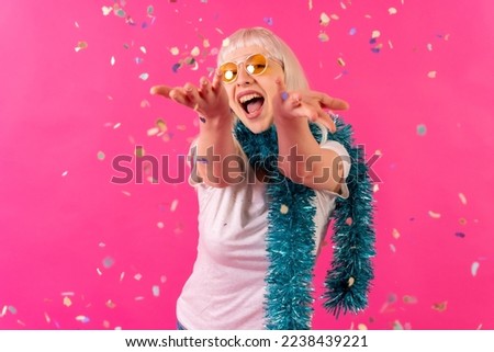 Smiling at a party throwing confetti in sunglasses, blonde caucasian girl on pink background studio