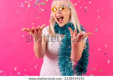 Very happy and smiling at confetti party wearing sunglasses, blonde caucasian girl on pink background studio