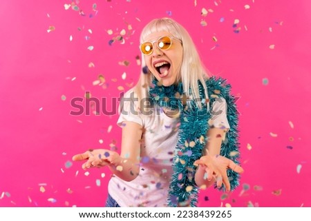 Smiling at a party throwing confetti in sunglasses, blonde caucasian girl on pink background studio