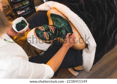 to view of an attractive blond woman at the spa getting a facial mask procedure by a specialist. High quality photo