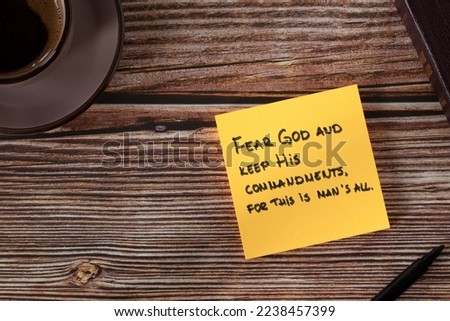 Fear God and keep His commandments, handwritten verse on yellow note with bible book and coffee cup on wooden table. Top view. Obedience and faith Christian biblical concept.