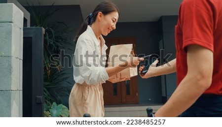 Young happy Asian woman accept paper bag from delivery man with bicycle in red uniform carry case box scan QR code payment on smartphone in front of house. express food delivery concept. Royalty-Free Stock Photo #2238485257