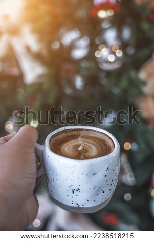 Close up holding of Hot coffee latte with latte art milk foam in cup mug with Xmas decors and Xmas tree baubles background,Celebrating Merry Christmas and New year.