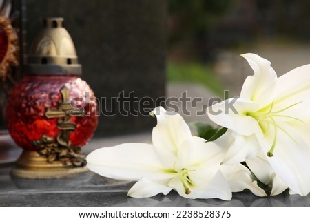 White lilies and grave light on grey granite tombstone outdoors, closeup. Funeral ceremony Royalty-Free Stock Photo #2238528375