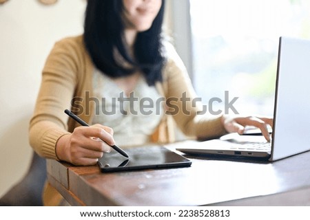 cropped image, An Asian female remote working at the coffee shop using laptop and tablet. side view