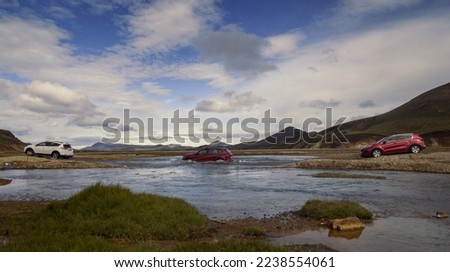 Cars driving across shallow river landscape photo. Beautiful nature scenery photography with mountains on background. Idyllic scene. High quality picture for wallpaper, travel blog, magazine, article