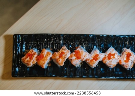 Flat lay or top view photo of a set of Tobiko sushi in a long black plate on a wooden table