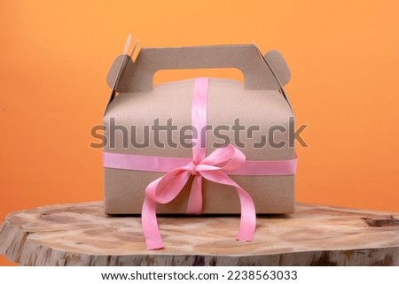 Craft a gift box with small pink ribbon on wood on orange background. Eco-friendly New Year and Christmas decoration concept
