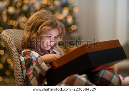 Surprise kid opening Christmas present gift box. Little kid celebrating Christmas or New Year near Christmas tree at home.