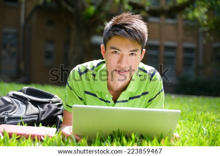Young male college student lying on use laptop at campus 