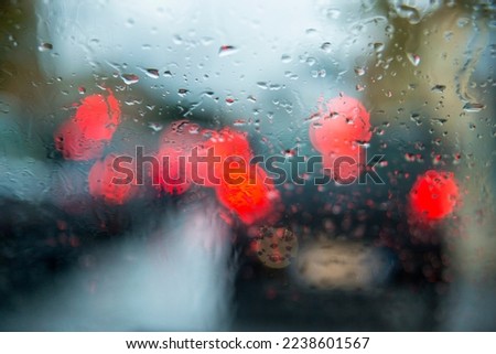 Wet glass of a car with raindrops in the foreground. In the background the car headlights in bokeh.