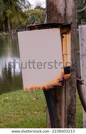 Rusty electric box with a blank  opened door next to a lake in a park