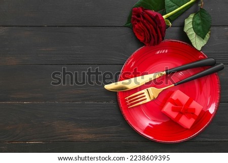 Table setting for Valentine's Day with gift and rose on black wooden background