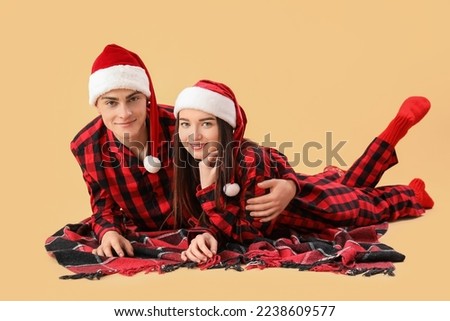 Young couple in Santa hats and pajamas lying on beige background