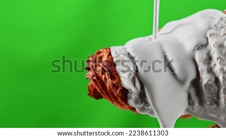 Trickling sweet white chocolate glaze covering small croissant. Stock clip. Pastry product isolated on a green chroma key background.
