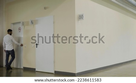 Young man walking inside the public bathroom inside shopping mall. HDR. Man entering toilet room.