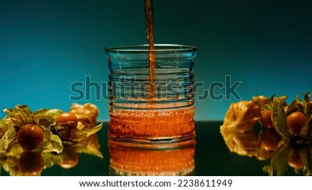Close up of pouring fruit drink inside an empty glass. Stock clip. Bar counter decorated by small yellow berries on the background of a wall with changing lights.