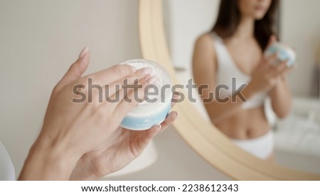 Women 's rest . Action . A beautiful young woman model in underwear who puts white cream on her body and poses next to a mirror.