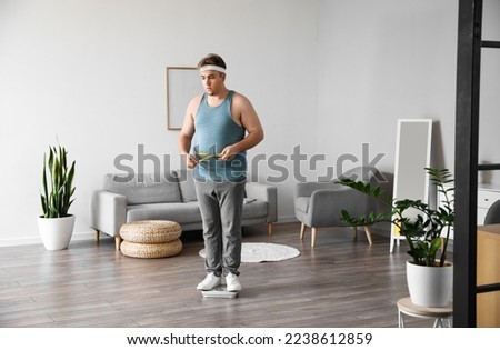 Young overweight man with measuring tape at home Royalty-Free Stock Photo #2238612859