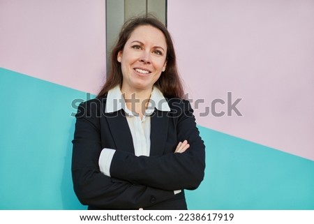 Happy smiling businesswoman with arms crossed leaning on colorful wall