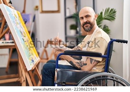 Young bald man artist sitting on wheelchair drawing at art studio